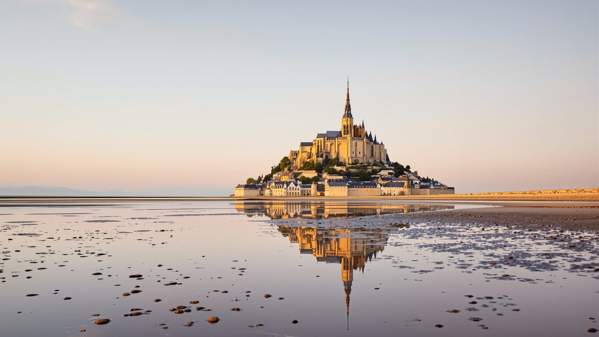 Le Mont-Saint-Michel et son abbaye au soleil couchant, reflétés dans la baie